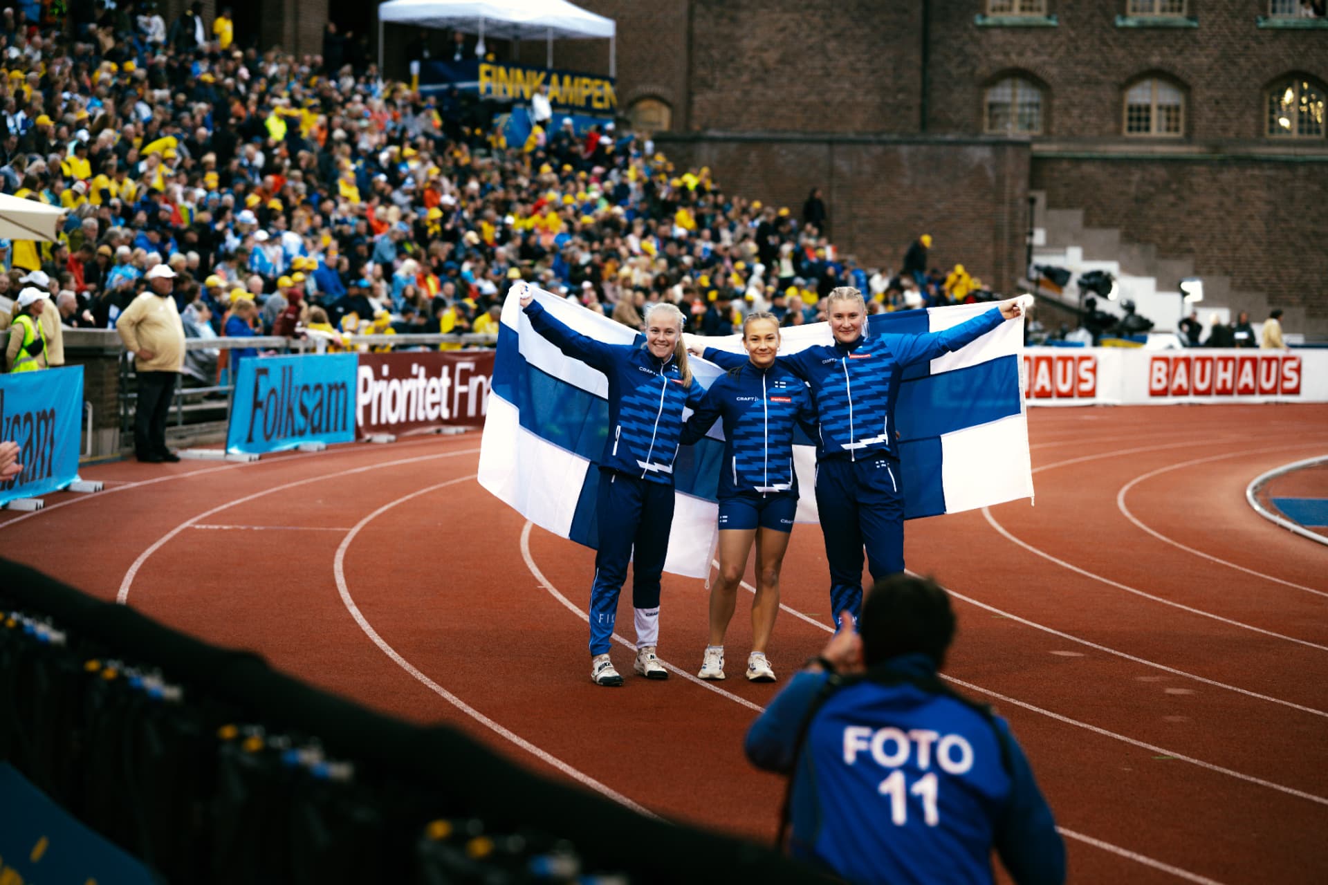 Suomen urheilijat juhlivat Suomen lipun kanssa radalla